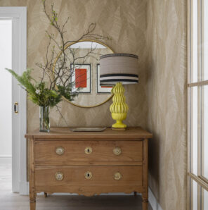 Recibidor con cómoda clásica de madera, lámpara amarilla de diseño y espejo redondo en vivienda familiar reformada en Getxo