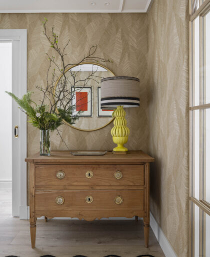 Recibidor con cómoda clásica de madera, lámpara amarilla de diseño y espejo redondo en vivienda familiar reformada en Getxo