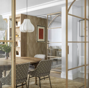 Cocina con península de mármol, cerramiento de madera con cristal y taburetes dorados, en reforma integral realizada en Algorta