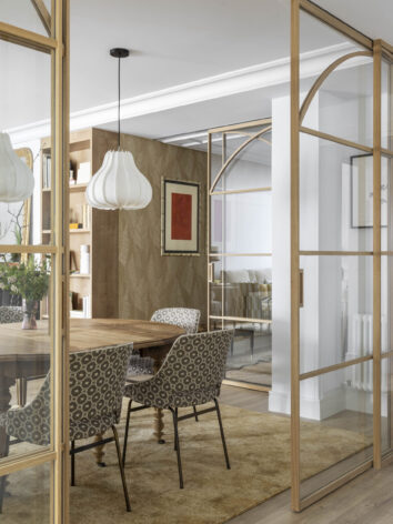 Cocina con península de mármol, cerramiento de madera con cristal y taburetes dorados, en reforma integral realizada en Algorta