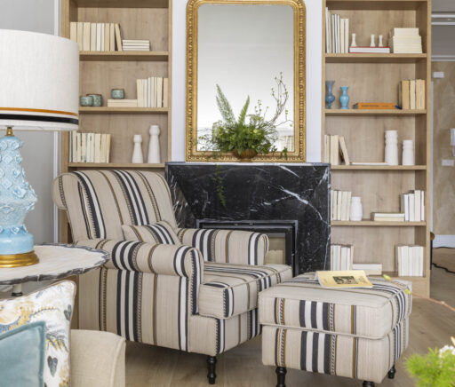 Rincón de lectura con sillón a rayas beige y negro, alfombra mostaza y espejo dorado, en salón reformado con estilo clásico actualizado