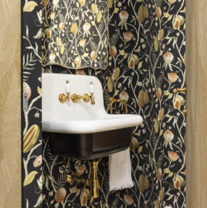 Aseo de cortesía con papel pintado floral en tonos oscuros y lavabo de estilo retro con grifería dorada en vivienda ecléctica de Getxo