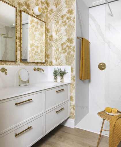 Mueble de baño doble blanco con tiradores dorados, espejos enmarcados y papel pintado vegetal en reforma integral de vivienda familiar